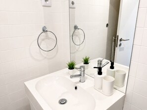 Een moderne badkamer met een witte wastafel, chromen kraan en twee kleine planten in potten.