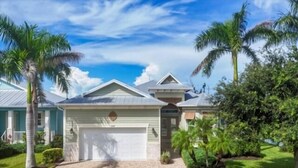 Une maison à deux étages avec un garage, entourée de palmiers et d’une pelouse bien entretenue.