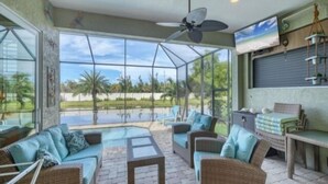 Un espace extérieur abrité, aménagé avec des meubles en osier, une table en verre et un ventilateur de plafond.