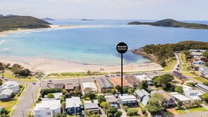 An aerial view of a coastal area with a beach, houses, and a sign for McGrath Nelson Bay Accommodation. - The Salty Sailor, 7 Market St - Wi-Fi, Water views, Air Con, Boat Parking (Fingal Bay)