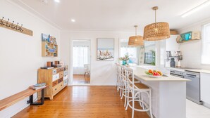 A modern kitchen with a central island, white bar stools, and pendant lighting. - The Salty Sailor, 7 Market St - Wi-Fi, Water views, Air Con, Boat Parking (Fingal Bay)