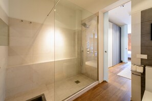 Une salle de bain moderne avec une douche à l’italienne en verre, une pomme de douche visible et un plancher en bois.