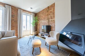 Un salon avec un mur en briques, une cheminée, un téléviseur et un canapé.