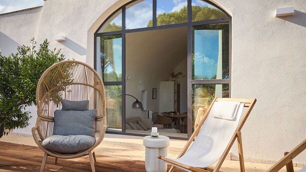 A wicker chair with cushions and a wooden lounge chair on a wooden deck.
