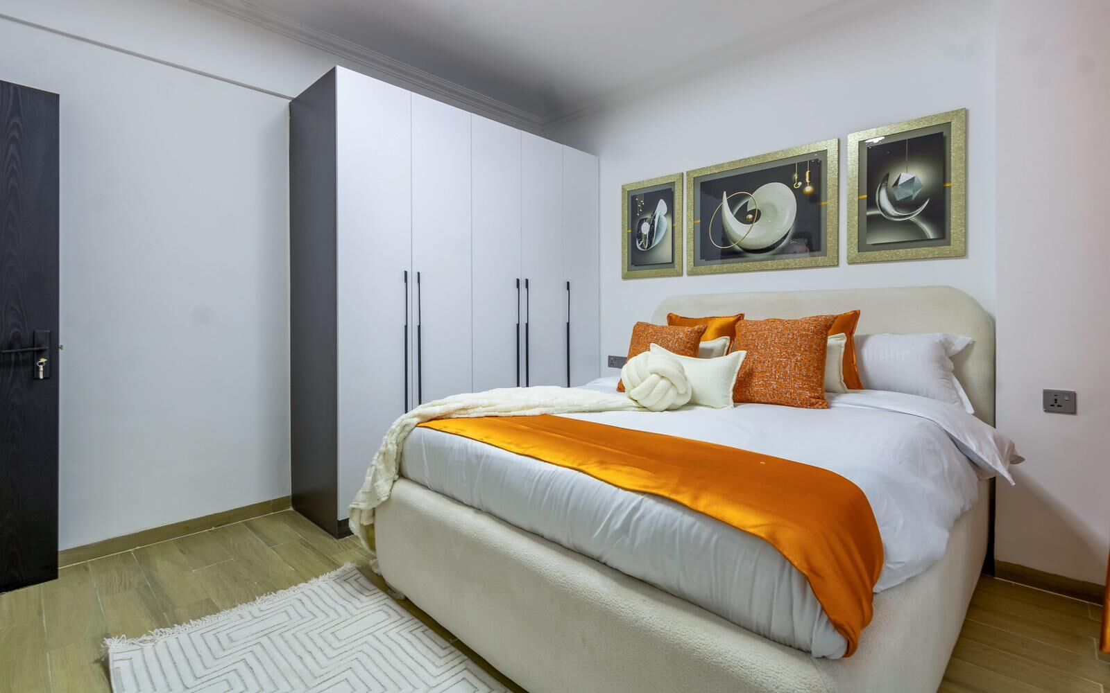 A bedroom with a bed, a wardrobe, and three framed artworks on the wall.