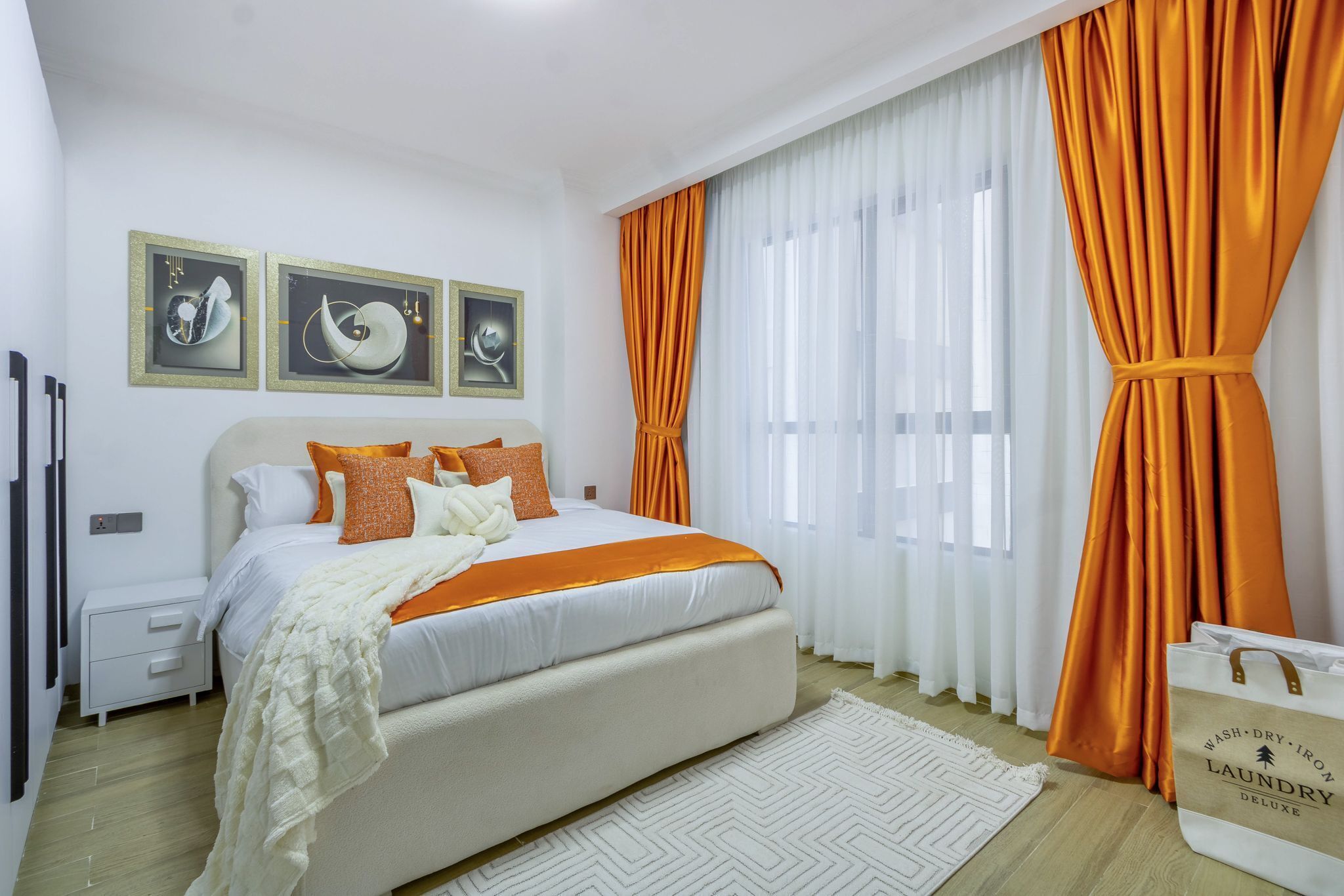 A bedroom with a bed, white curtains, and orange drapes.