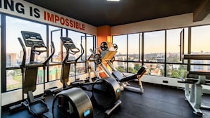 Une salle de sport équipée de machines de cardio, de matériel de musculation et de grandes fenêtres donnant sur la ville.