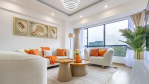 Un salon moderne comprenant un canapé, des fauteuils, une table basse et une grande fenêtre donnant sur la ville.
