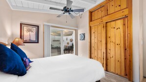 Une chambre à coucher comprenant un lit, un ventilateur de plafond, une armoire en bois et une porte donnant sur un balcon.