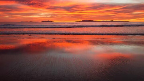 Une plage aux eaux calmes où se reflète le ciel au coucher du soleil.