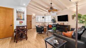 A spacious living room with a ceiling fan, a dining area with a wooden table and chairs, a black leather sofa, and a television mounted on the wall. - 25% Off 30+ Stay! Steps To Sand, Great Location (Oxnard)