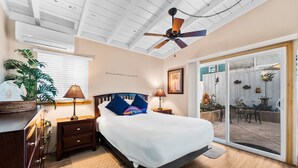 A bedroom with a bed, bedside tables, a ceiling fan, a window with blinds, and a view of an outdoor patio with chairs and plants. - 25% Off 30+ Stay! Steps To Sand, Great Location (Oxnard)