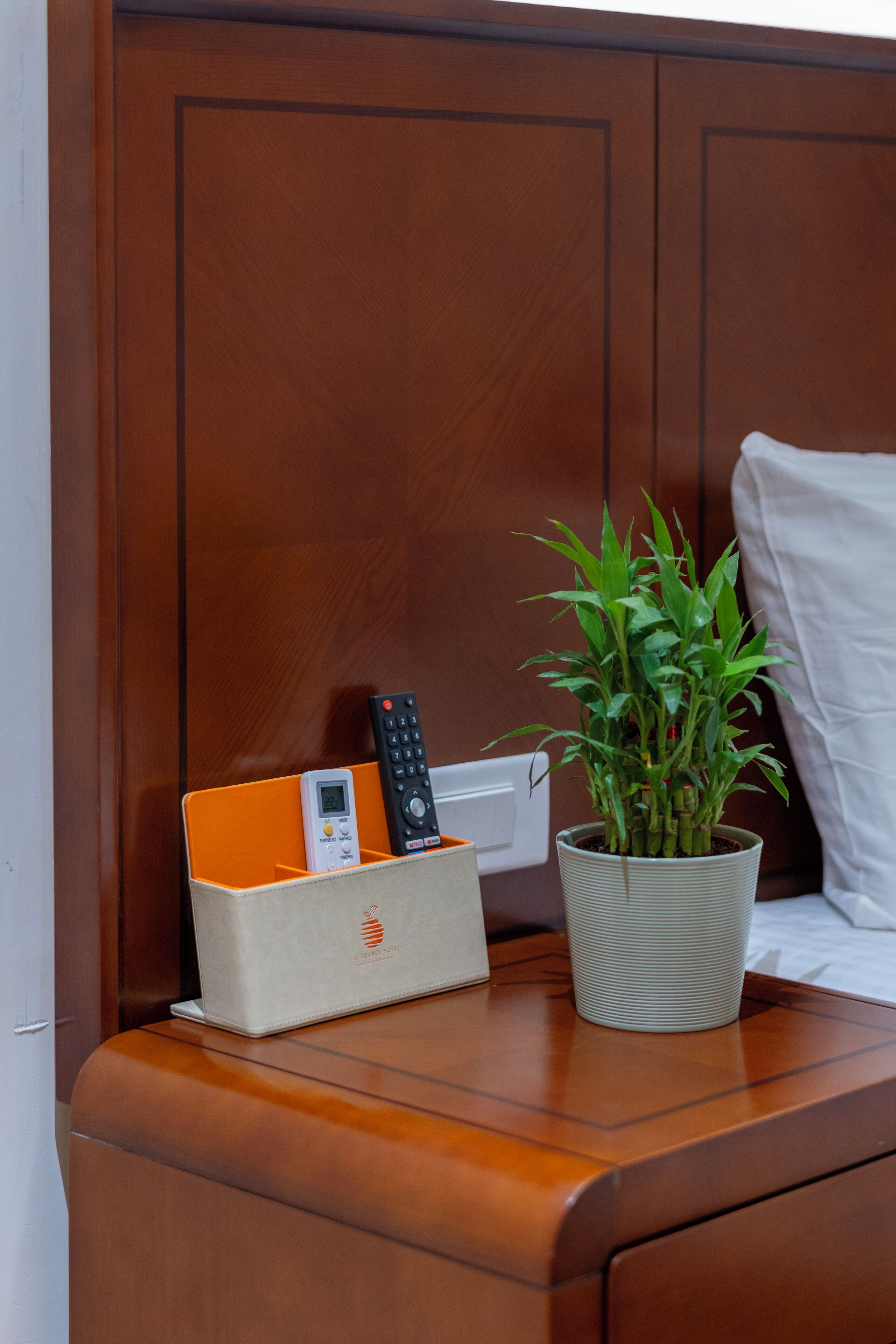 A wooden bedside table with a remote control, a smartphone, and a potted plant.