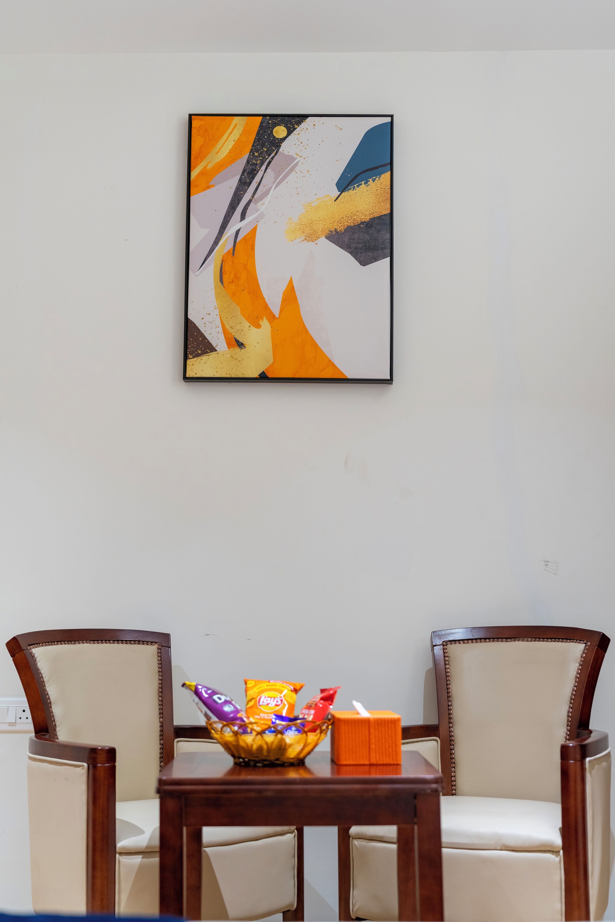 Un comedor con dos sillas, una mesa con aperitivos y un cuadro abstracto colgado en la pared.