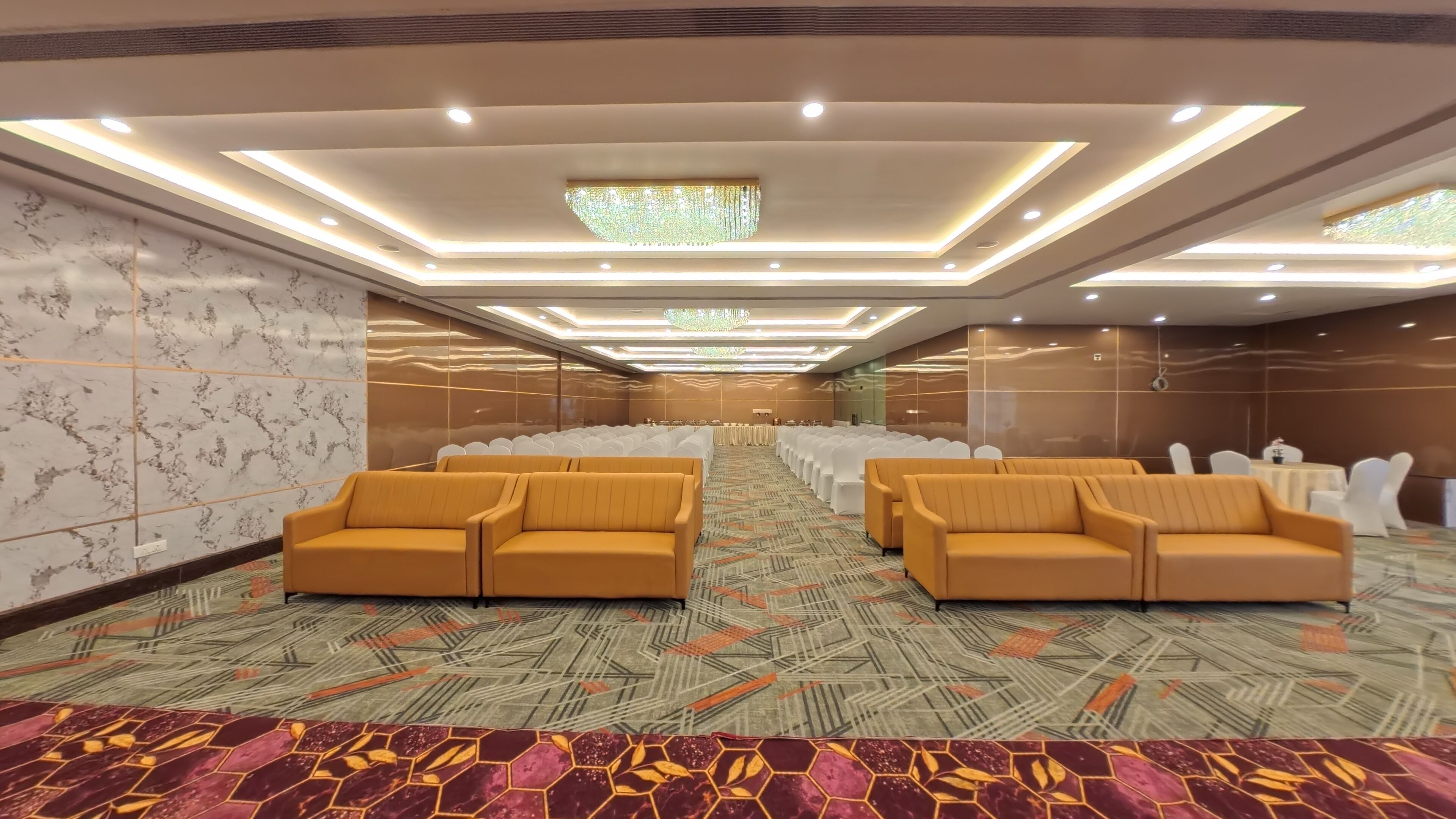 Un salón de conferencias con filas de sillas blancas, un escenario central y sofás amarillos.