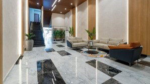Un hall d’entrée moderne avec un sol en marbre à carreaux, deux canapés, une table basse et un escalier en arrière-plan.