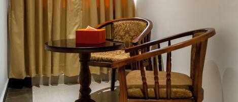 A room with a round wooden table, a chair, a red box, and a framed abstract artwork on the wall.