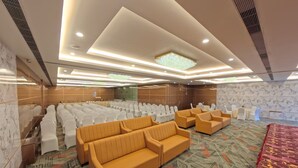 Une salle de conférence avec des rangées de chaises blanches, des canapés orange et une moquette à motifs.