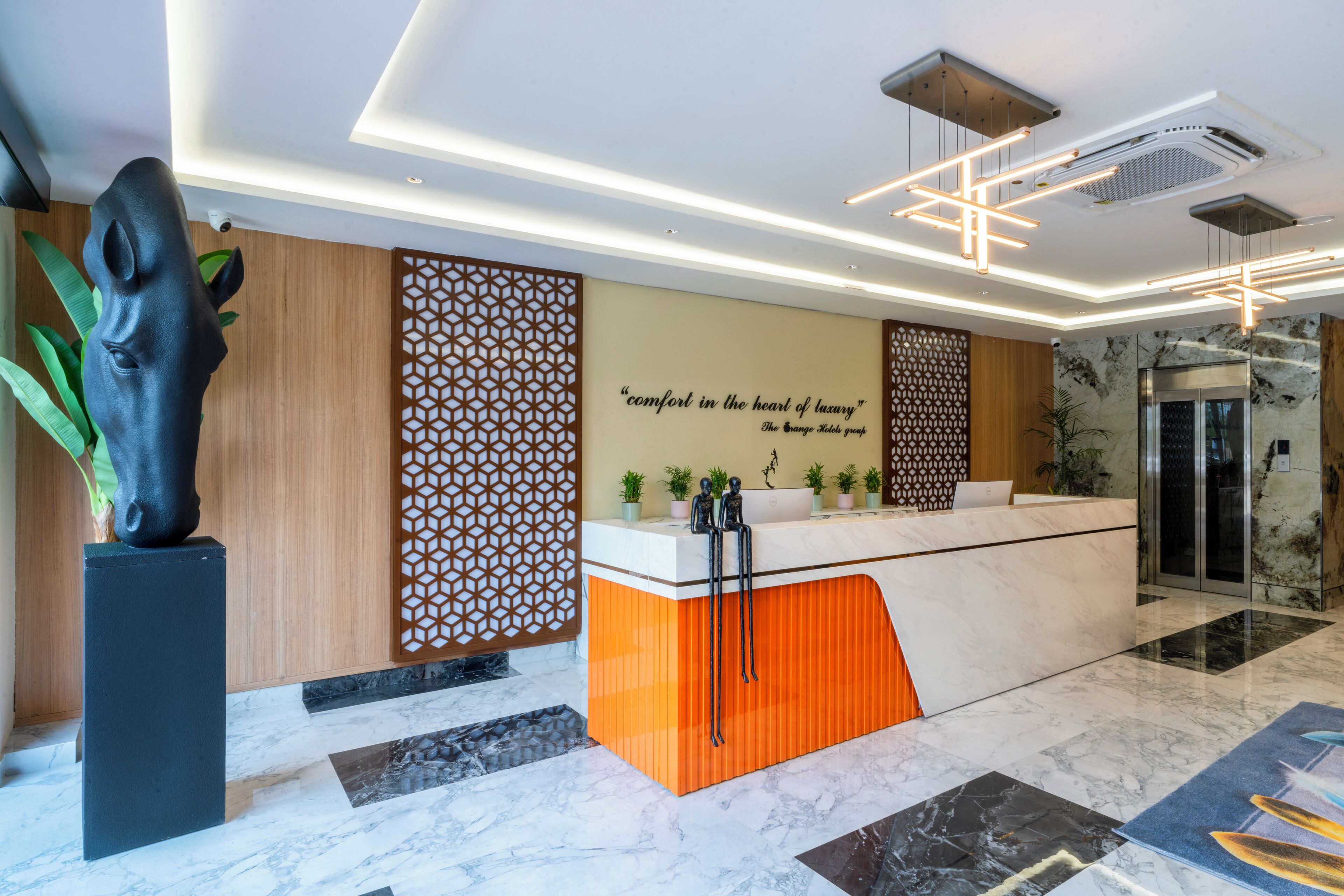 Zona de recepción de un hotel con diseño moderno, que incluye un mostrador, paneles decorativos y una gran escultura.