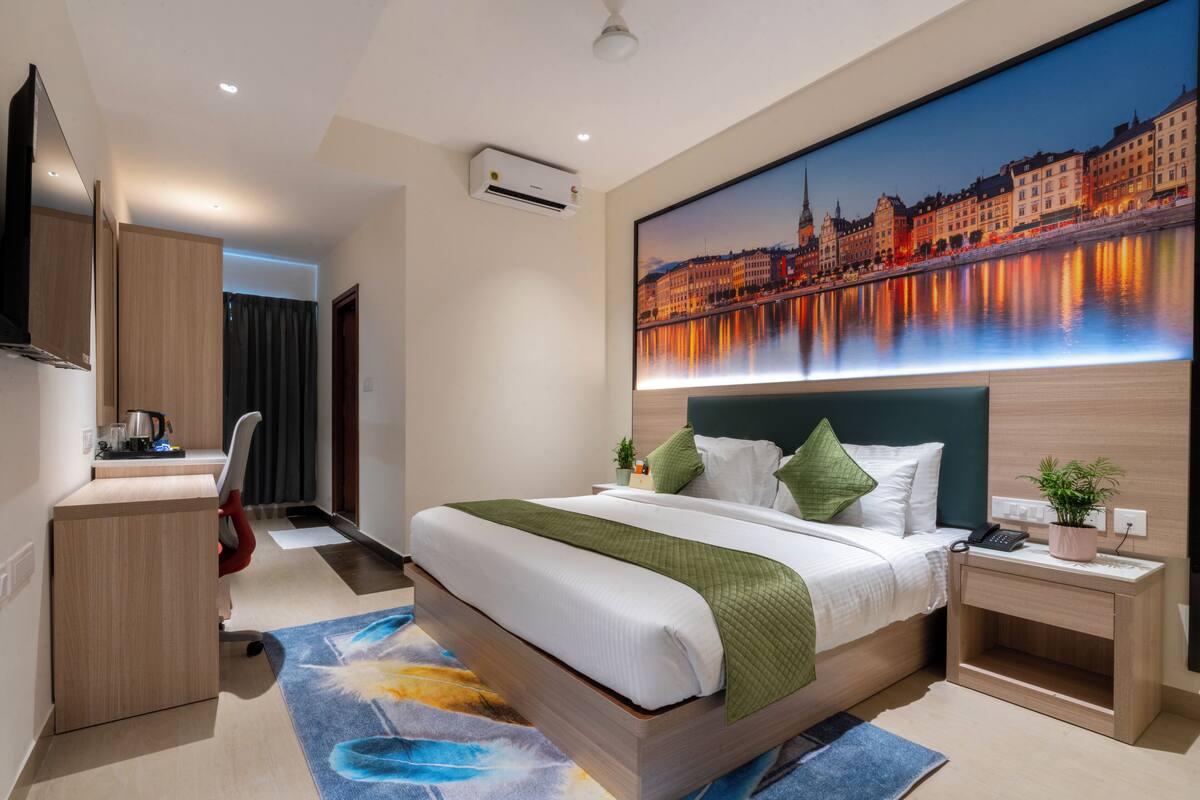Une chambre d’hôtel moderne avec un grand lit, un bureau et un tableau représentant un paysage urbain accroché au mur.