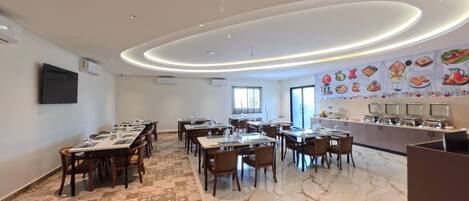 A modern dining area with multiple tables and chairs, a kitchen counter with appliances, and a mural depicting food items on the wall.