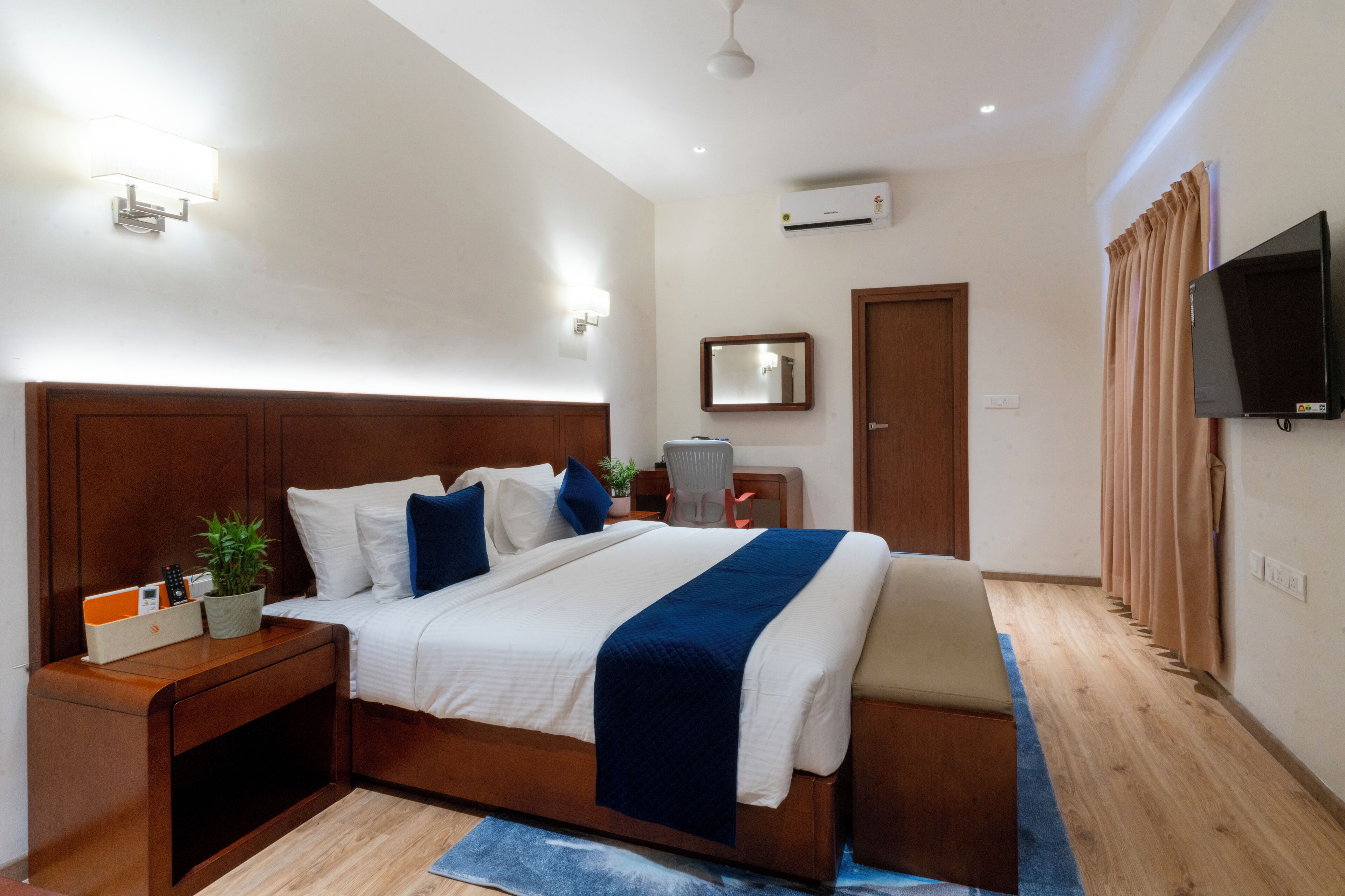 A neatly arranged bedroom with a large bed, bedside tables, a TV, and a mirror.