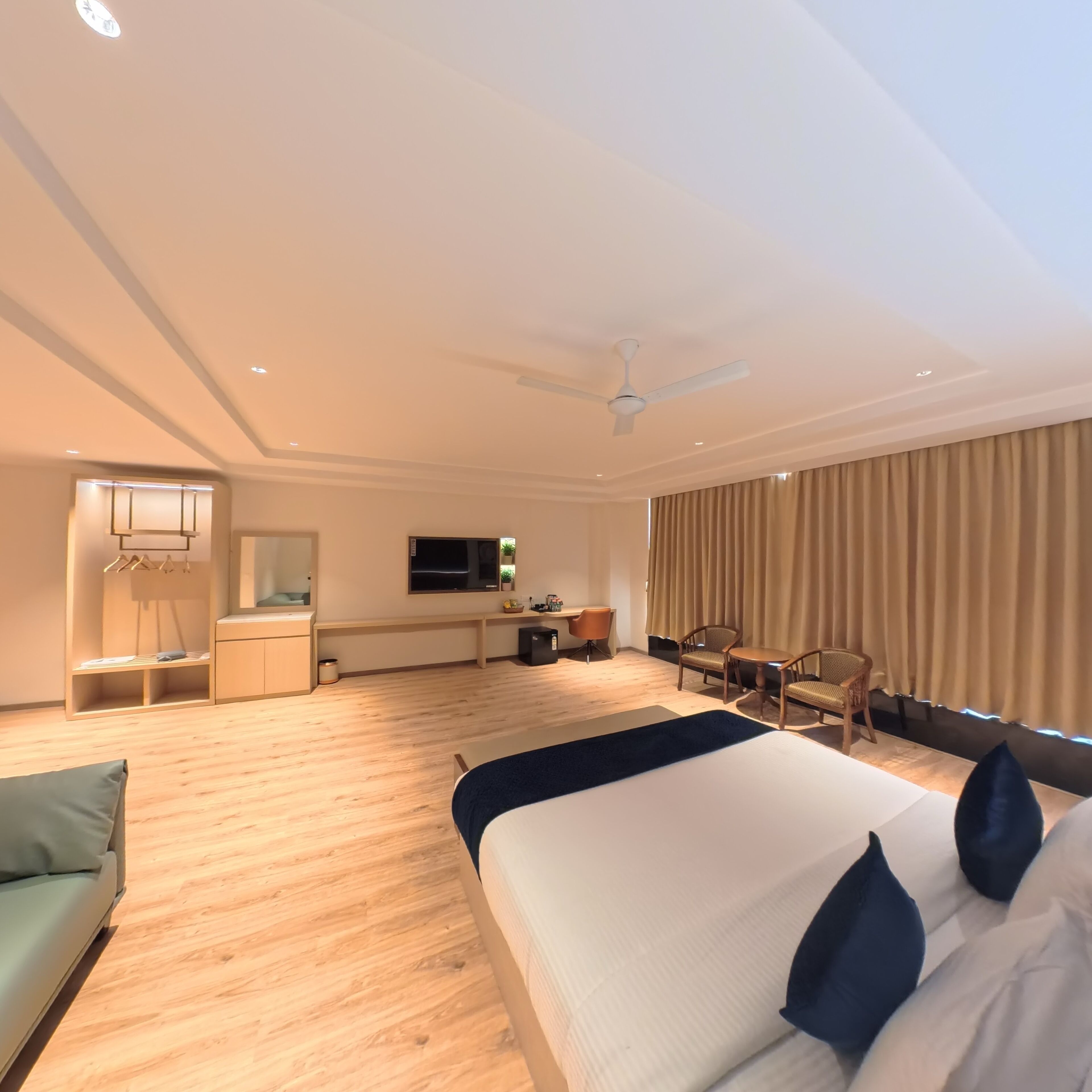 A hotel room with a large bed, a desk, a chair, a wardrobe, and a ceiling fan.