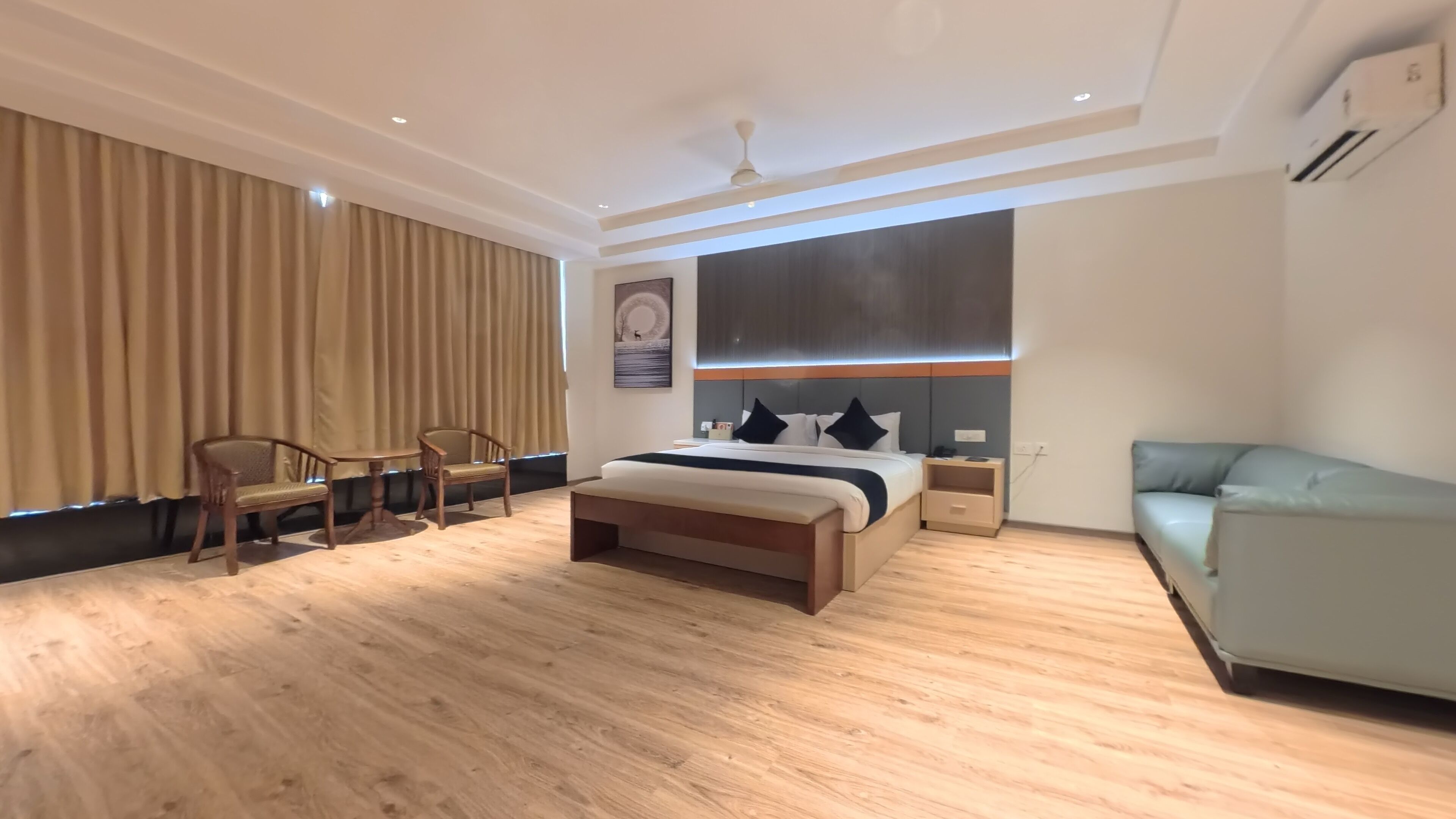 A modern hotel room with a large bed, a seating area with two chairs, a sofa, and a ceiling fan.