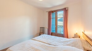 Une chambre à coucher avec un lit, une chaise, une fenêtre avec des rideaux et une table de chevet avec une lampe.