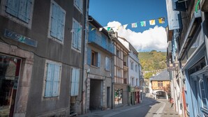 Une rue étroite, bordée de bâtiments des deux côtés, dont certains présentent des devantures de magasins et des enseignes visibles.