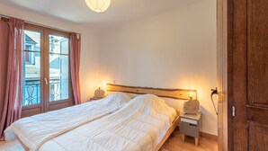 Une chambre à coucher avec un lit, des lampes de chevet, une tête de lit en bois, une table de chevet et une vue sur l’extérieur par une fenêtre avec des rideaux.