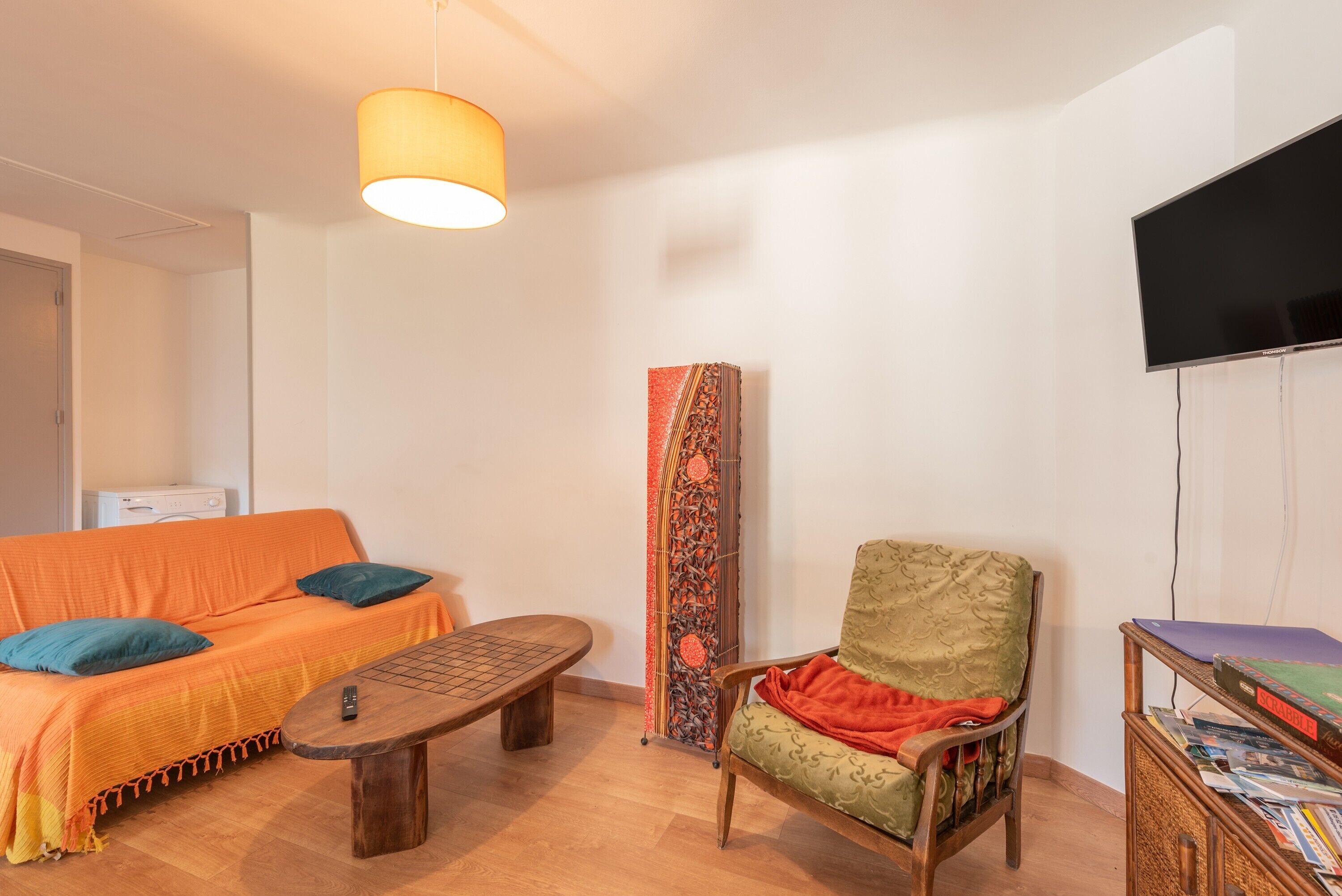 Une pièce comprenant un canapé, un fauteuil, une table, une lampe, un téléviseur et une bibliothèque.