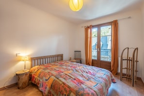 Ein Schlafzimmer mit einem hölzernen Bett, einem Nachttisch mit Lampe, einem Fenster mit Vorhängen und einer Holzleiter.