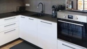 Uma cozinha moderna com armários brancos, bancada preta, máquina de café e forno.