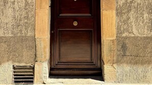 A dark wooden door with a brass knocker, set in a stone wall with a small vent below. - Family Housing (2 Adults + 1 Child) - Center City (MIREPOIX)