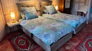 A double bed with floral bedding, two bedside lamps, and a red patterned rug. - Family Housing (2 Adults + 1 Child) - Center City (MIREPOIX)