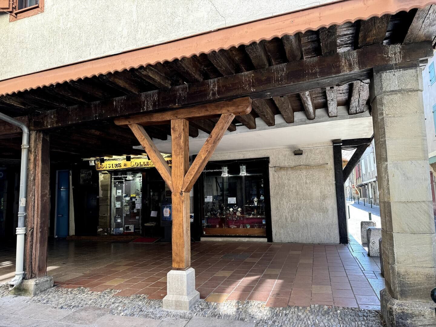 A covered outdoor area with a wooden structure, a tiled floor, and a shop with glass display windows.
