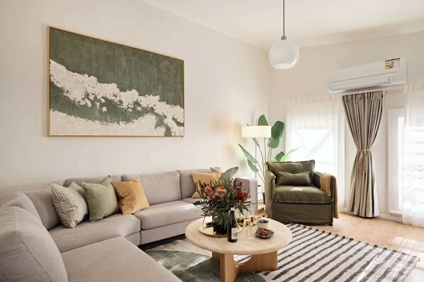 Un salon avec un canapé, un fauteuil, une table basse ornée de fleurs et un tableau accroché au mur.
