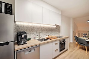 Une cuisine moderne avec des meubles blancs, un pare-feu à motifs, une machine à café, une planche à pain et un coin repas avec une table et des chaises.