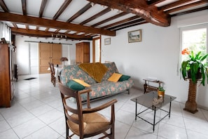 A room with a sofa, wooden chairs, a table, a potted plant, and a window.