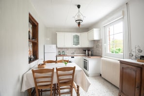 A kitchen with white cabinets, a dining table with chairs, a hanging light fixture, and a window with a view.