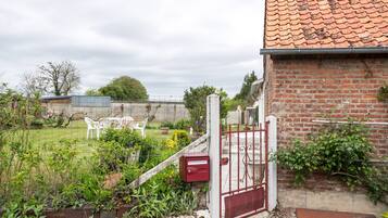 A fenced garden with a brick wall, a red gate, and a white chair.