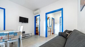 A modern living room with a grey sofa, a dining table with chairs, a flat-screen TV, and blue-framed doors leading to other rooms. - Apartment 'De Playa' with Sea View, Balcony and Air Conditioning (Calafell)