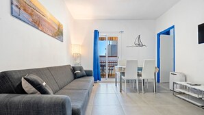 A modern living room with a sofa, dining table, chairs, and a kitchen area. - Apartment 'De Playa' with Sea View, Balcony and Air Conditioning (Calafell)
