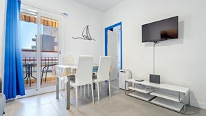 A modern room with a dining table, chairs, a TV, and a sliding glass door leading to an outdoor area. - Apartment 'De Playa' with Sea View, Balcony and Air Conditioning (Calafell)