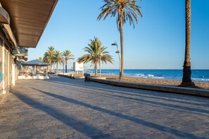 Un camino pavimentado con palmeras, una playa y un edificio con un letrero que dice '112' al fondo.