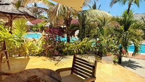An outdoor seating area with wooden furniture, a pool, and tropical plants. - Paje Blu Boutique Hotel (Paje)