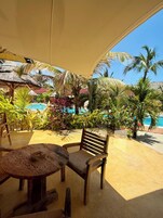 An outdoor seating area with wooden furniture, a pool, and tropical plants.