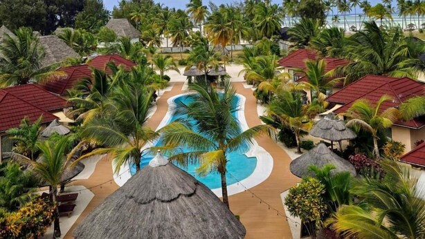 Ein Resort mit einem zentral gelegenen Schwimmbad, strohgedeckten Gebäuden und Palmen.