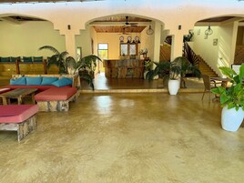 A spacious lobby with a wooden reception desk, a staircase, and multiple seating areas with cushions.